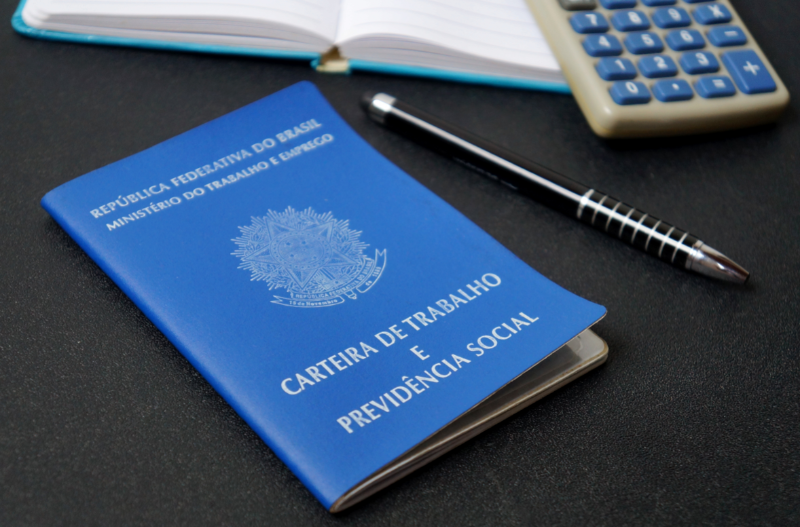 caderno calculadora caneta e carteira de trabalho e previdência social em cima de uma mesa ctps