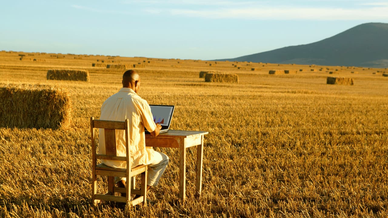Trabalhador no campo utilizando computador, simbolizando aposentadoria híbrida rural e urbana.